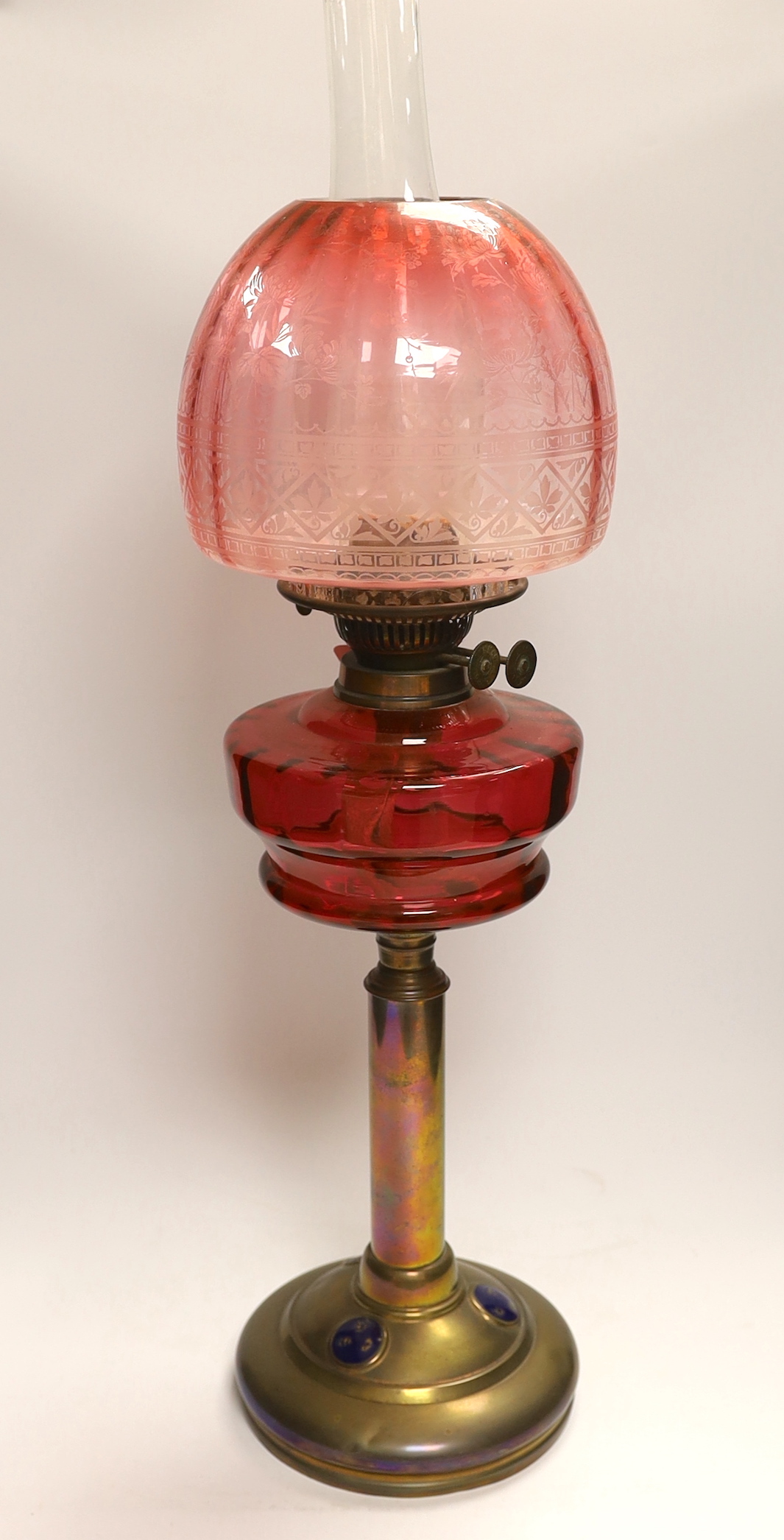 19th century brass oil lamp with cranberry glass reservoir, etched shade and Ruskin type cabochon panels to the base, 68cm high overall